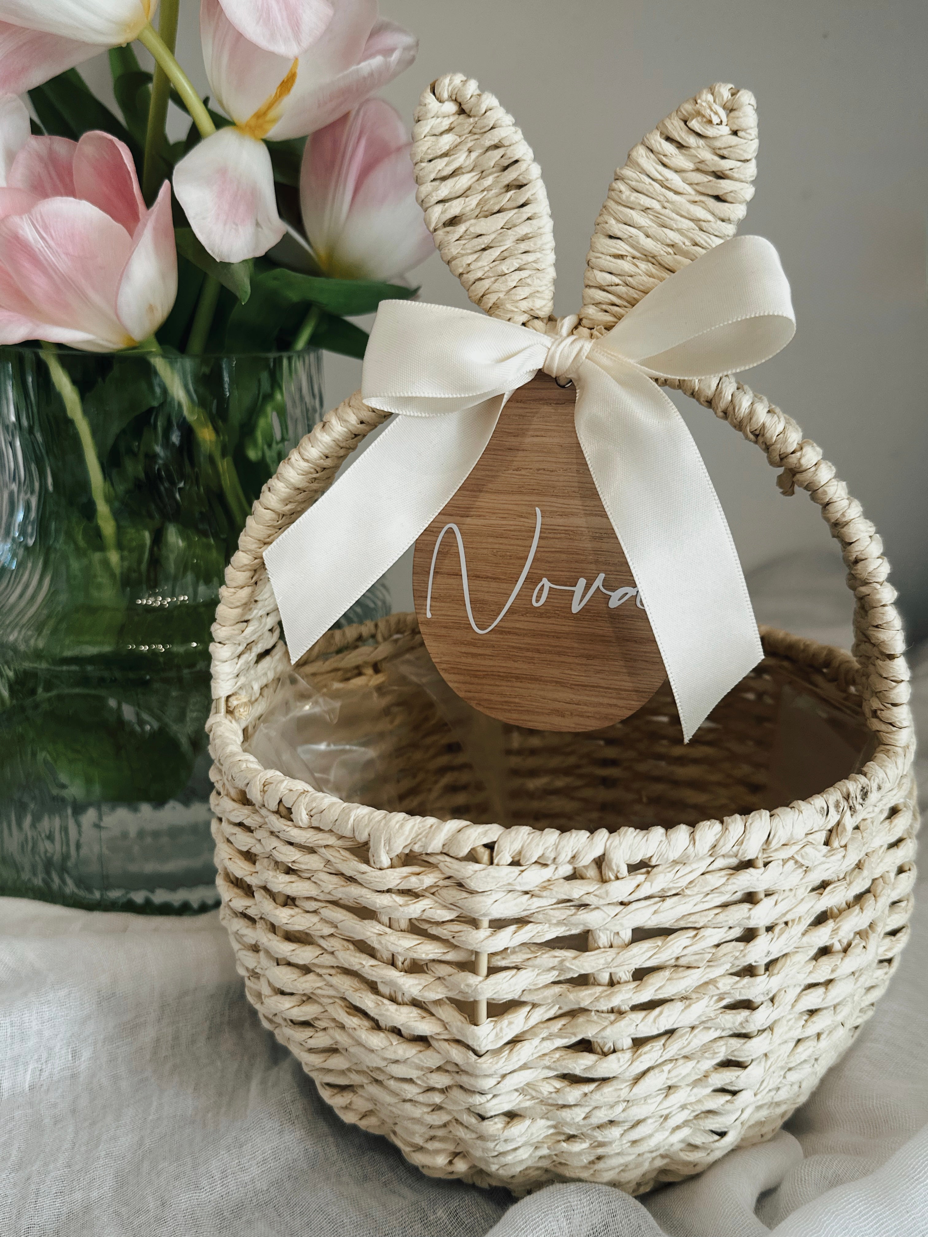 Woven basket with a wooden heart and bow, placed next to pink tulips in a vase.