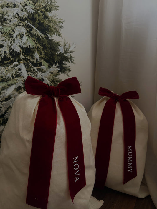 Natural-coloured Christmas gift sacks with burgundy bows personalised with Nova and Mummy