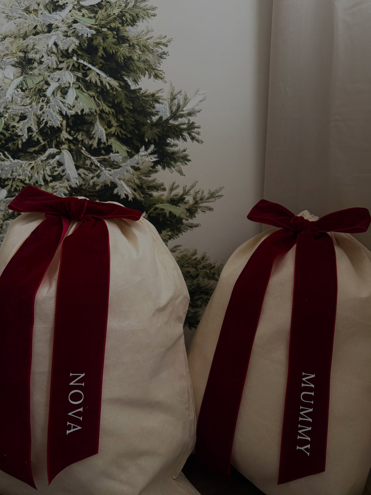 Close view of personalised burgundy bows on natural-coloured Christmas gift sacks