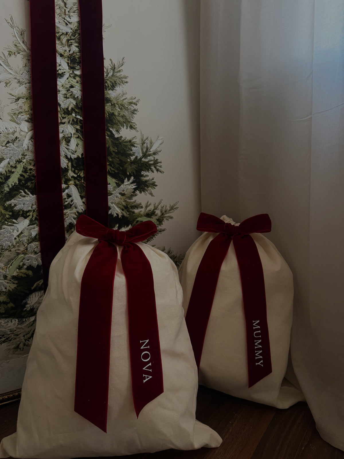 Personalised natural-coloured Christmas gift sacks styled beside a tree