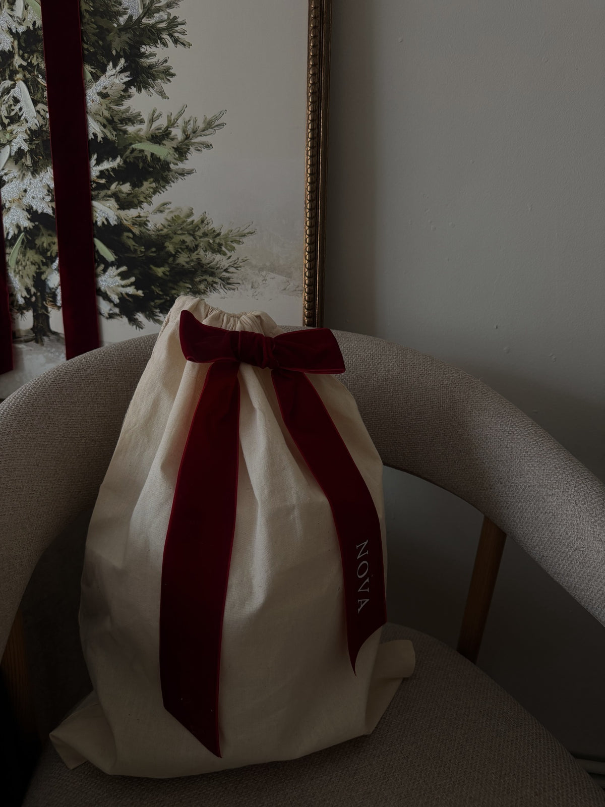 Natural-coloured Christmas gift sack with a burgundy bow on a chair